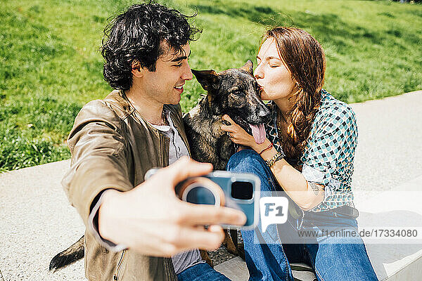 Mann nimmt Selfie durch Smartphone mit Frau küssen Hund während sonnigen Tag