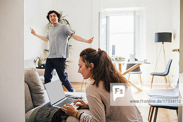Frau benutzt Laptop mit Mann tanzt im Hintergrund zu Hause