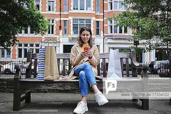 Frau sitzt auf einer Bank und benutzt ein Smartphone in der Stadt