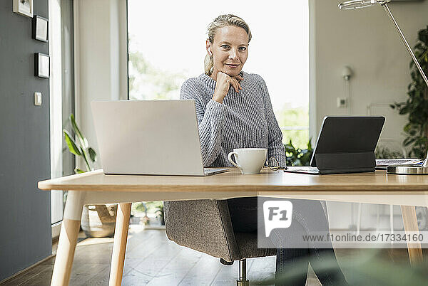 Geschäftsfrau mit Hand am Kinn sitzt am Schreibtisch im Büro