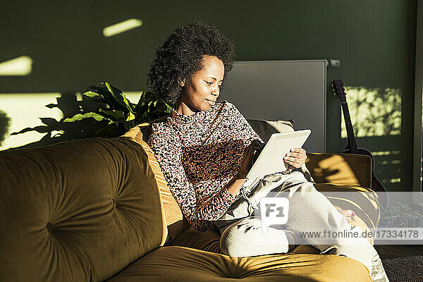 Frau benutzt digitales Tablet  während sie auf dem Sofa im Wohnzimmer sitzt