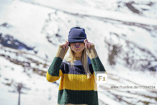 Woman covering eyes with knit hat on snowcapped mountain