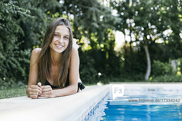 Lächelnde junge Frau mit braunen Haaren  die in den Ferien am Pool liegt