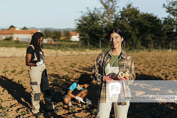 Lächelnde junge Bäuerin mit Radieschen auf einem Bio-Bauernhof an einem sonnigen Tag