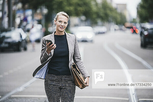 Female professional holding mobile phone and bag while walking at tramway