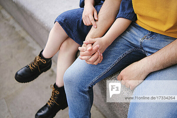 Young couple holding hands while sitting together on wall