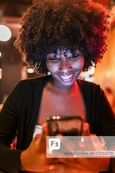 Lächelnde junge Frau  die in einer Bar ein Mobiltelefon benutzt