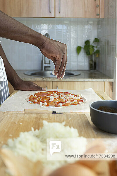 Mann belegt Pizza mit gehackten Zwiebeln in der Küche zu Hause