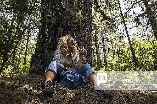 Lächelnde Frau hält Kaffeetasse im Wald sitzend