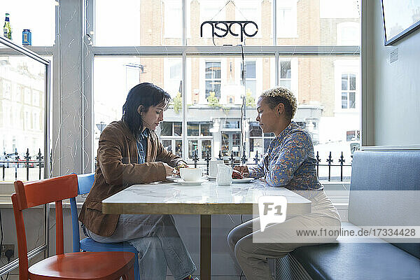 Lesbian couple sitting at table in cafe by glass window