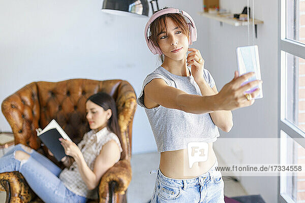 Female photographer taking selfie while colleague reading book in background