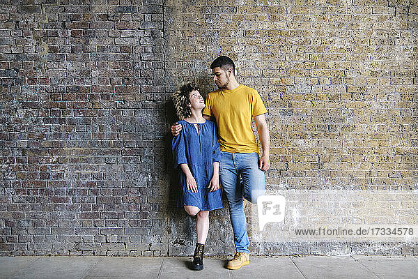 Young couple looking at each other while standing in front of wall