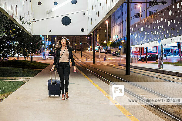 Geschäftsfrau  die ein Gepäckstück auf Rädern zieht  während sie nachts auf dem Bahnsteig geht