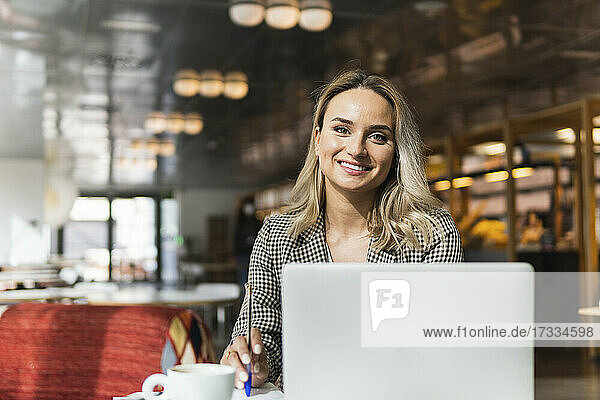 Lächelnde Geschäftsfrau hält einen Stift vor einem Laptop in einem Café