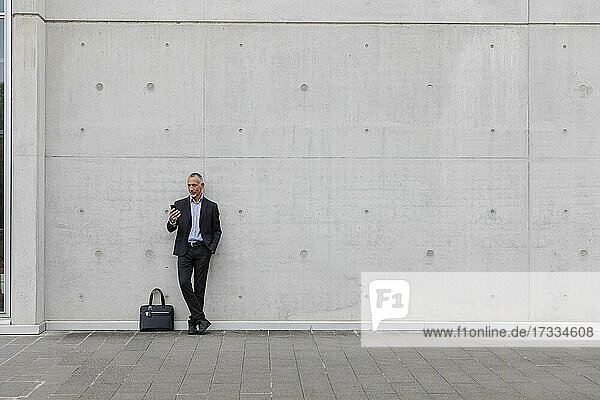 Male professional using smart phone while standing near wall