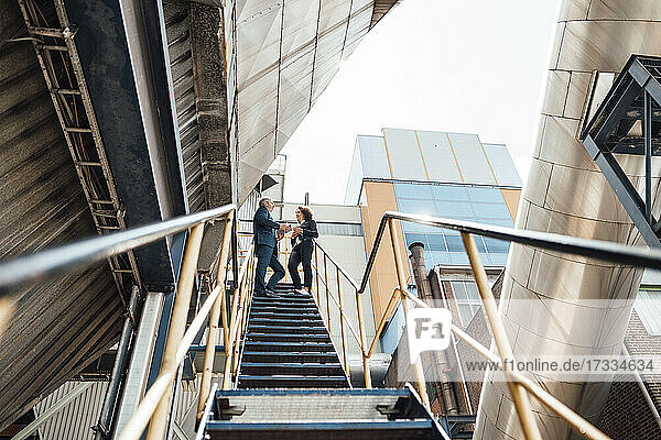 Geschäftsfrau im Gespräch mit einem Kollegen  während sie auf einer Treppe im Kraftwerk steht