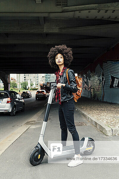 Junge Frau mit Elektroroller auf der Straße unter einer Brücke stehend