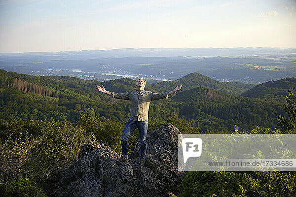 Male hiker with arms outstretched standing on top of mountain