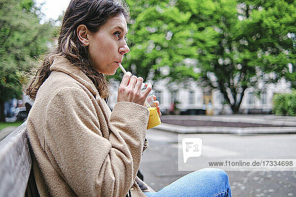 Nachdenkliche Frau  die einen Smoothie trinkt und auf einer Bank sitzt