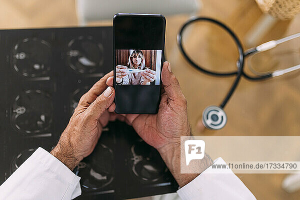 Weibliche Patientin zeigt einem männlichen Arzt während eines Videogesprächs in der Klinik ein Thermometer