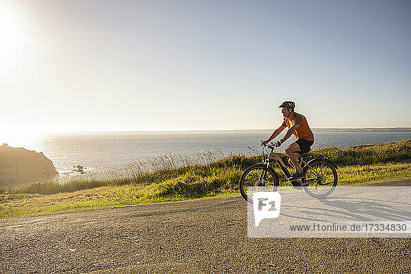 Mature sportsman cycling bicycle on road near sea at sunset
