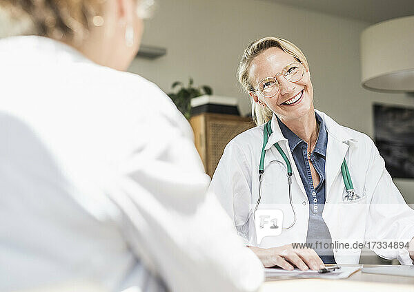 Weiblicher Arzt lächelt  während er einen Patienten im Büro betrachtet
