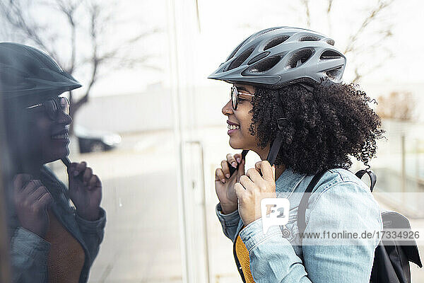 Smiling young woman looking at glass window while wearing cycling helmet