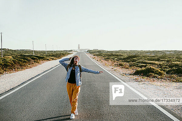 Smiling woman with arms outstretched walking on road