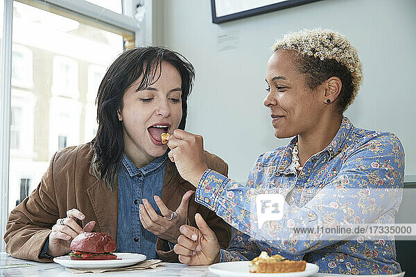 Lächelnde Frau füttert Freundin im Café sitzend mit Essen