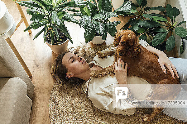 Young woman with Cocker Spaniel lying on rug at home