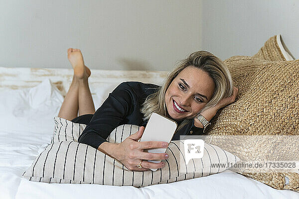Smiling female professional using smart phone while lying on bed at home