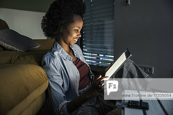 Frau lächelt  während sie ein digitales Tablet im Wohnzimmer benutzt