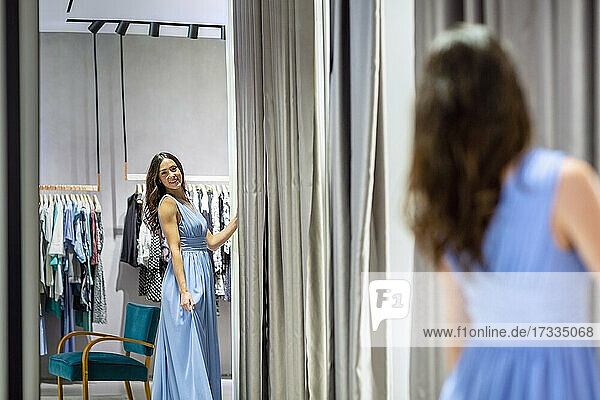 Frau schaut in den Spiegel und trägt ein blaues Kleid in einer Boutique