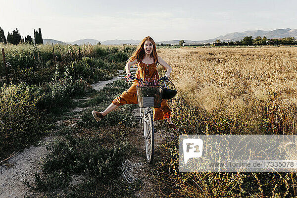 Unbekümmerte Frau fährt Fahrrad in einem landwirtschaftlichen Feld