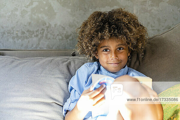 Cute boy with book sitting on sofa in living room