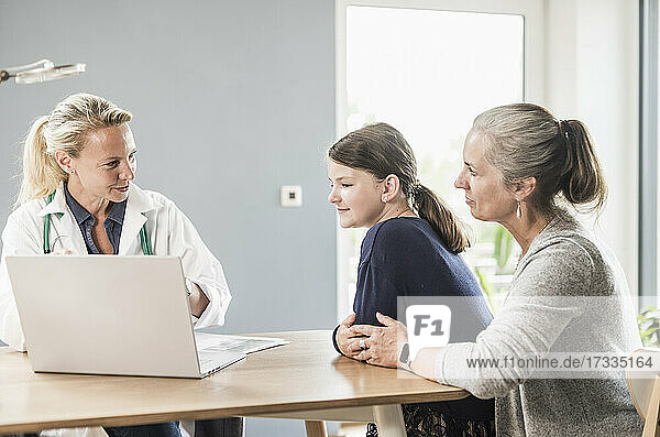 Kinderarzt erklärt Patientin und Frau mit Laptop in der Arztpraxis