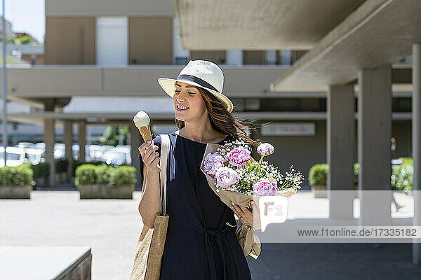 Frau hält Blumenstrauß  während sie in der Nähe eines Gebäudes ein Eis betrachtet