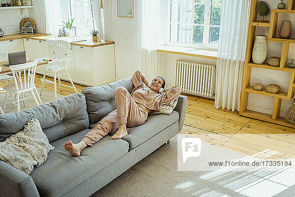 Lächelnde Frau auf dem Sofa liegend  während sie zu Hause nachdenkt
