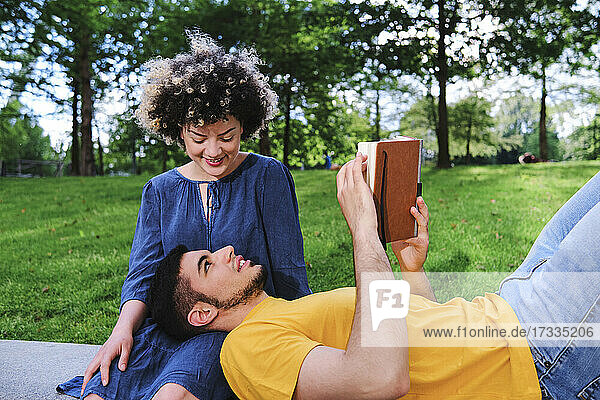 Lächelnde junge Frau sieht ihren Freund auf dem Schoß liegend im Park an