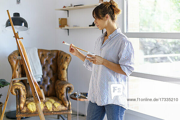Junge Malerin betrachtet im Atelier stehend ein Bild