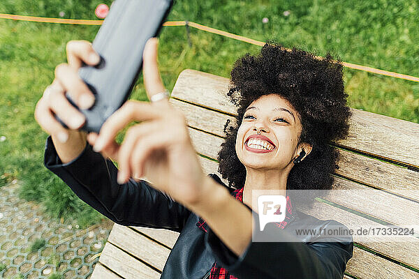 Glückliche Frau  die ein Selfie mit ihrem Mobiltelefon macht  während sie auf einem Stuhl im Park liegt