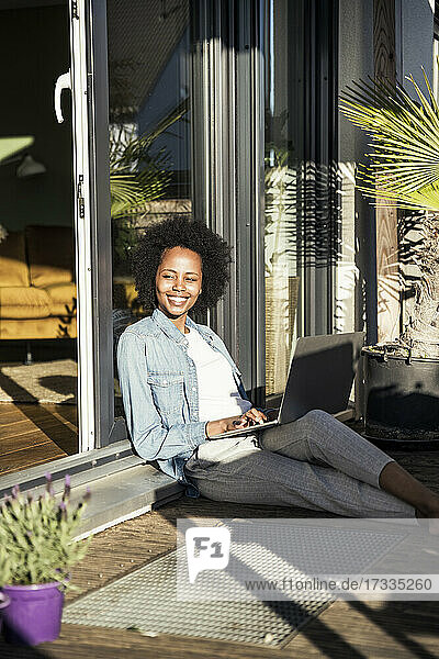 Lächelnde Frau  die einen Laptop benutzt  während sie auf dem Balkon sitzt