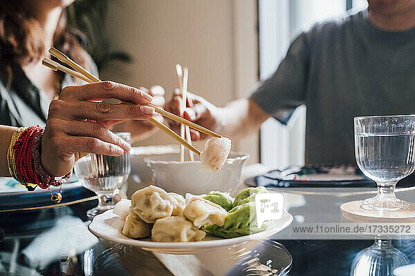 Woman taking food with chopsticks while sitting by man at home