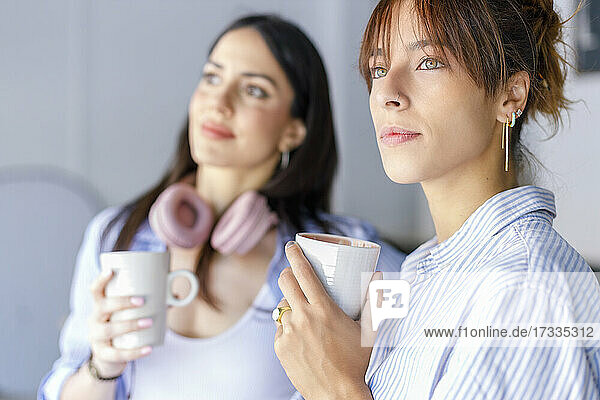 Contemplating female creative colleagues looking away holding mugs in studio