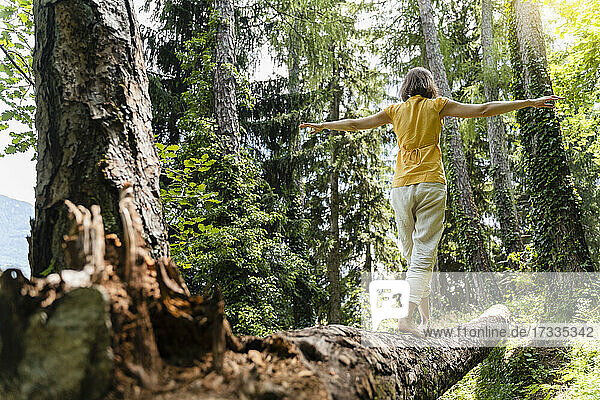Frau mit ausgestreckten Armen auf umgestürztem Baum im Wald gehend