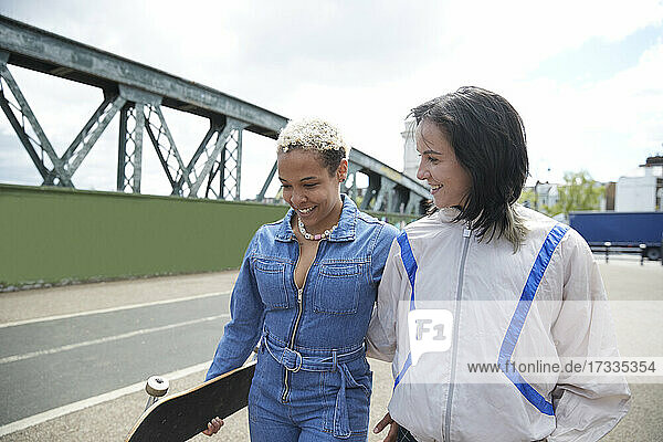 Smiling woman looking at girlfriend while walking on bridge