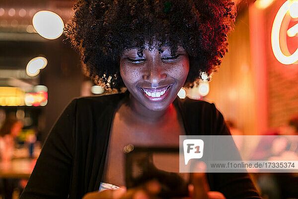 Afro-Frau lächelt bei der Benutzung eines Mobiltelefons in einer Bar