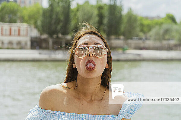 Woman wearing sunglasses sticking out tongue in front of river