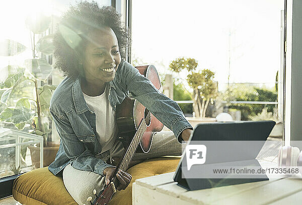 Frau mit Gitarre  die ein digitales Tablet benutzt  während sie zu Hause sitzt