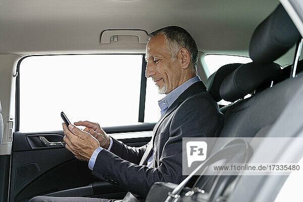 Businessman using smart phone while sitting on back seat in car